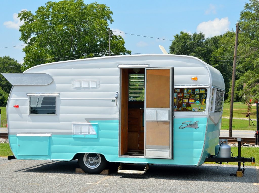 A small white and turquoise camper trailer with an open door