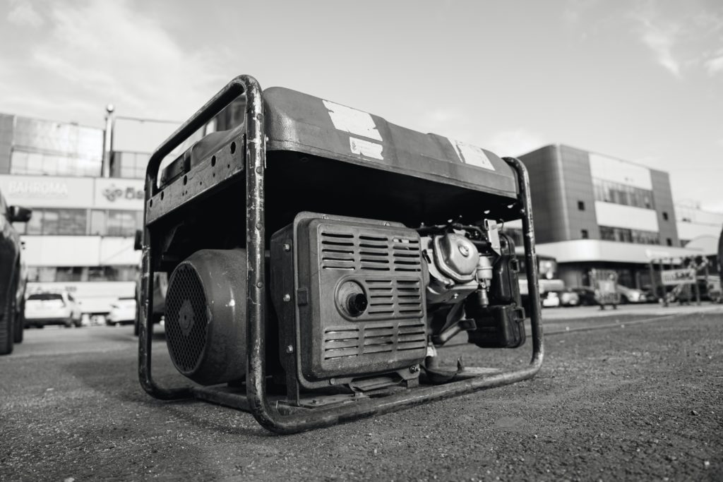 A generator sits on the pavement on a city street with buildings in the background.
