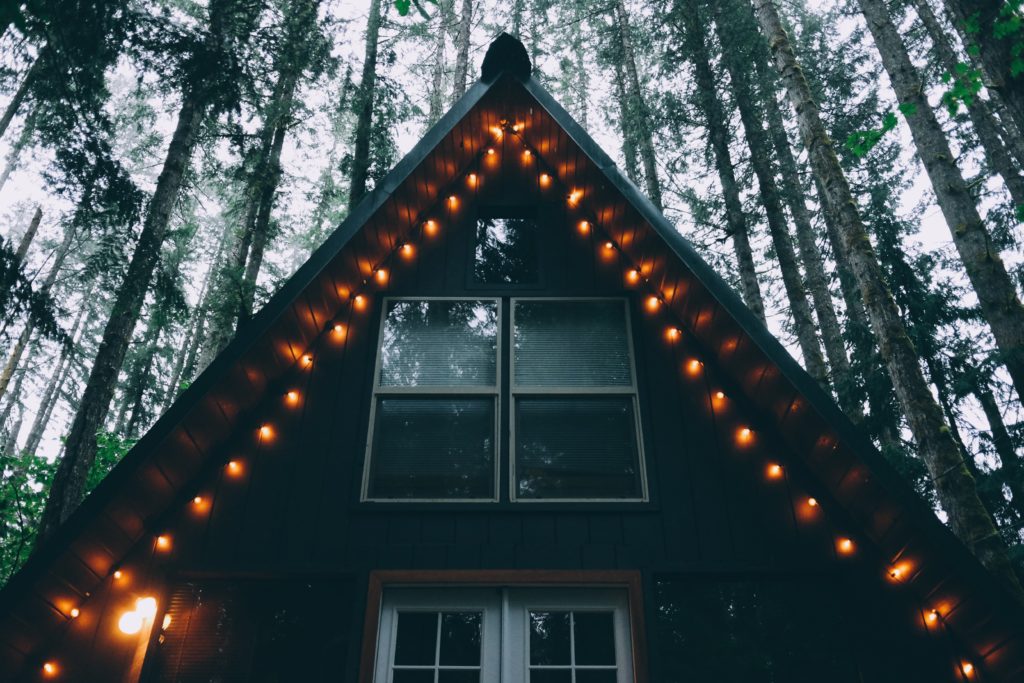 Lights line the eave of an A-frame cabin with trees in the background.